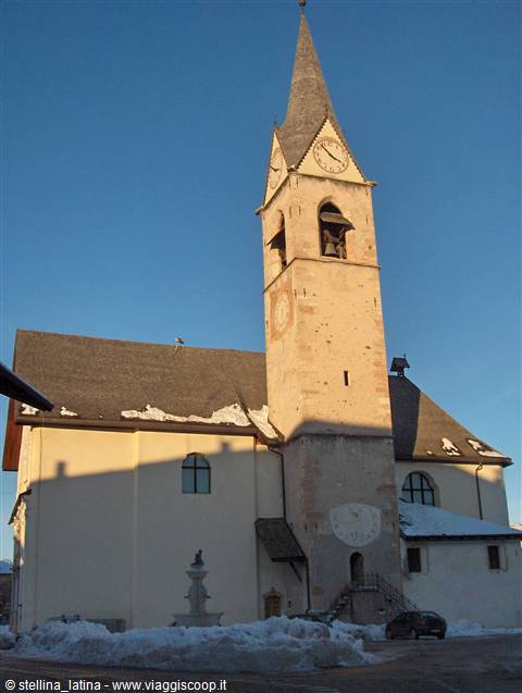 Stone bell tower with clock and bell, snowy church under clear blue sky