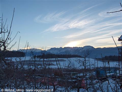 Snowy fields and mountains at dawn, bare branches and greenhouses in the valley