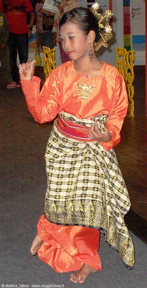 Girl dances in traditional songket costume, orange tunic and golden jewelry