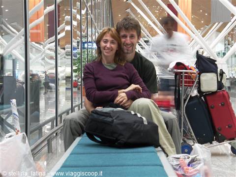 couple with backpack and suitcases sitting on baggage carts belt at airport