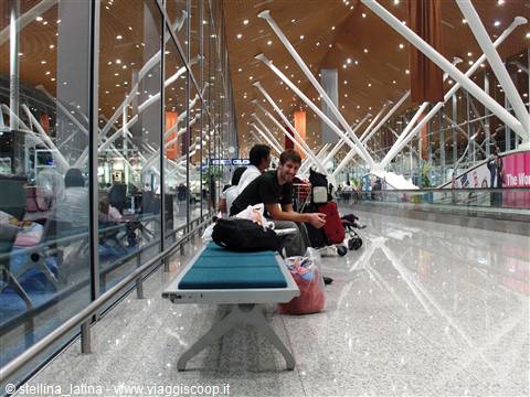 Traveler with backpack seated on bench, white structure of Kuala Lumpur airport