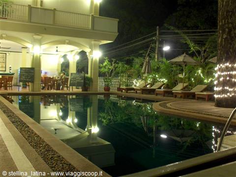 Lit hotel pool at night beside arcade with umbrellas and loungers