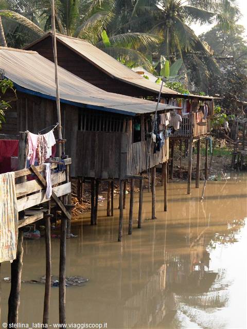 Wooden stilt houses along the river, laundry hanging, palm trees