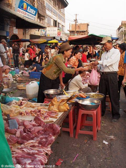 Busy street market: vendor hands meat to a customer among stalls and red stools