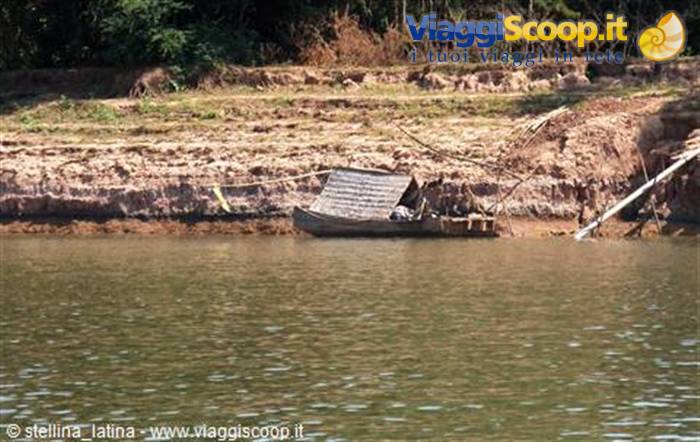 Wooden boat with canopy moored by eroded riverbank, calm green water
