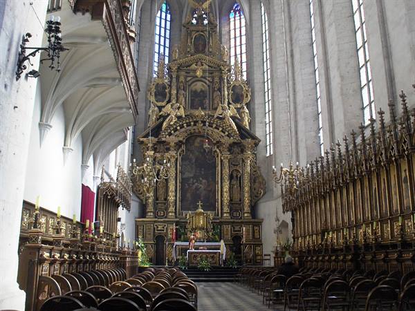 Gothic interior with gilded baroque altar, statues and wooden chairs