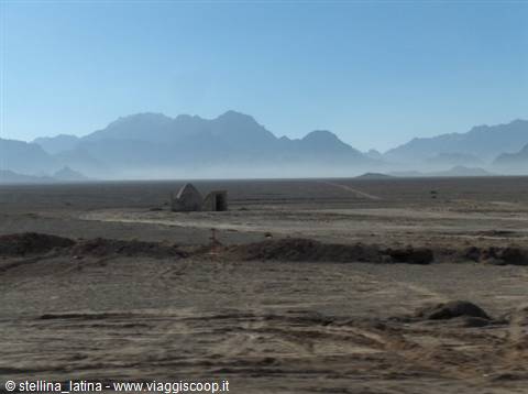 Small brick hut in the desert, hazy blue mountains rising behind