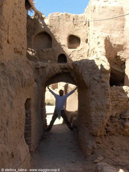 Man posing under a mud-brick arch in crumbling earthen village ruins