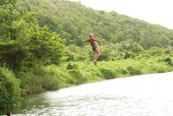 Man in swim trunks leaping into river surrounded by green forested hills
