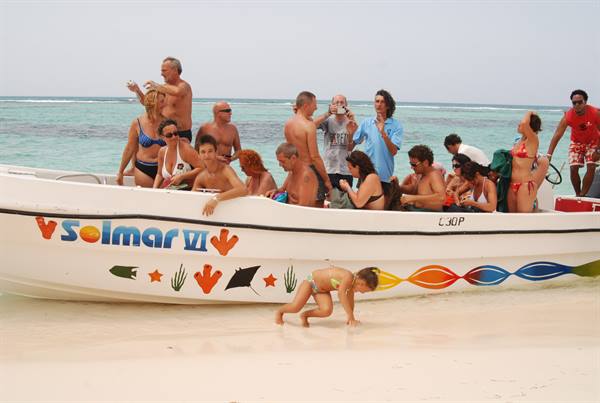 Tourists in swimwear on Solmar VI boat, toddler in bikini on sand