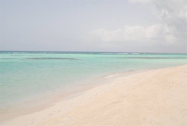 White sand and turquoise water under cloudy sky, gentle waves on shore