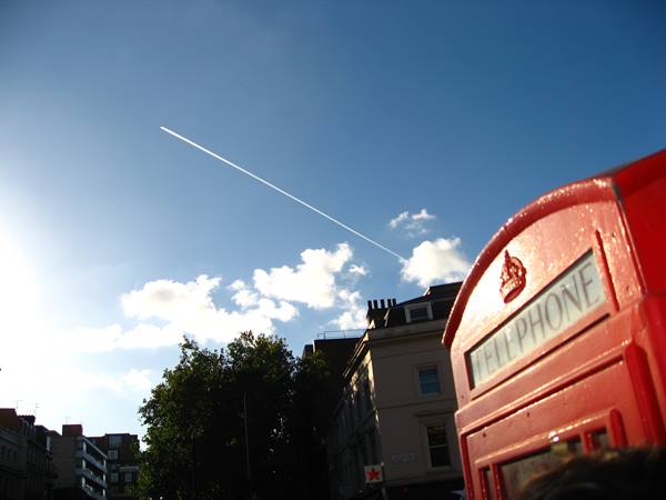 Red London telephone box under blue sky with an airplane contrail