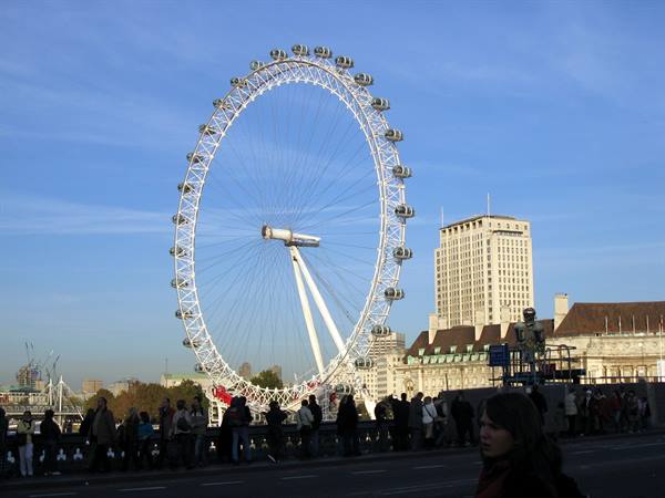 The London Eye's white wheel against blue sky, tourists crowding the bridge