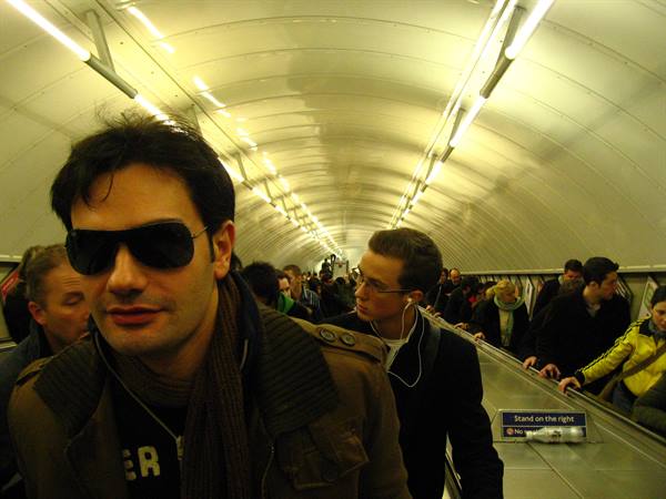 Man in dark sunglasses on crowded subway escalator, lit tunnel