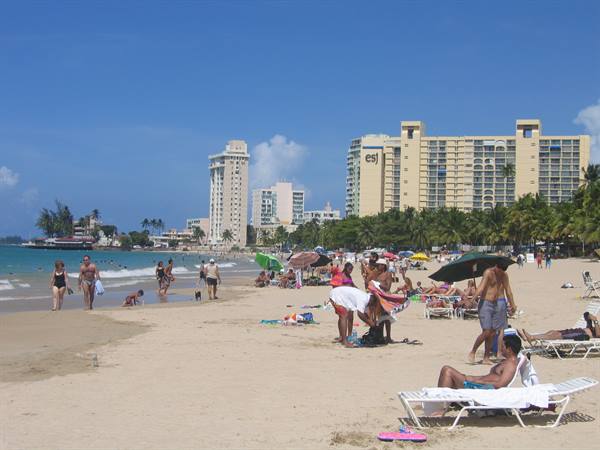 Beachgoers under umbrellas on the sand, Condado high-rises and palms