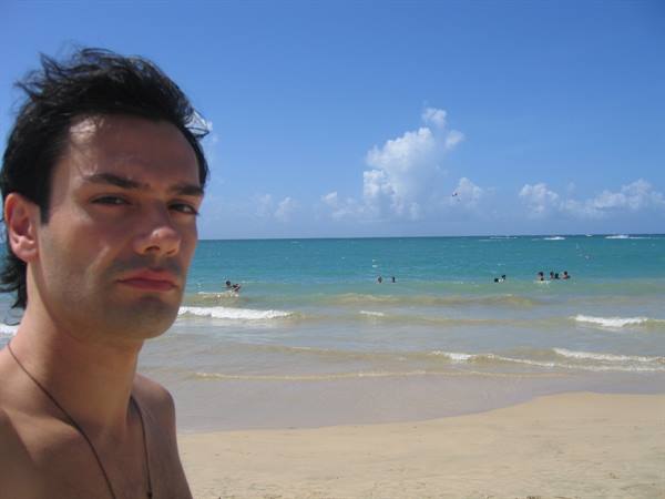 Young man on light sand beach, swimmers in turquoise sea under blue sky