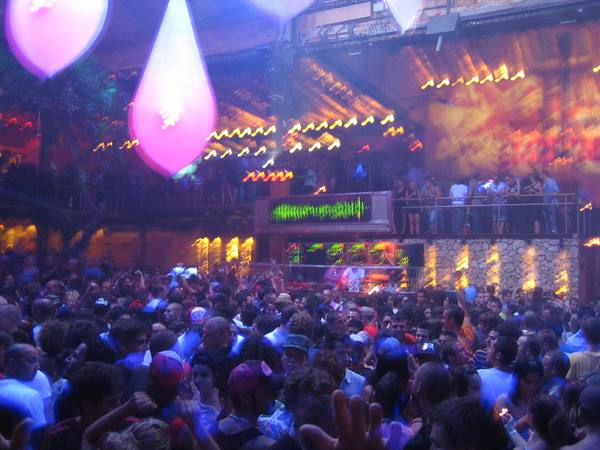 Crowd dancing at an open-air club with colorful lights and glowing balloons