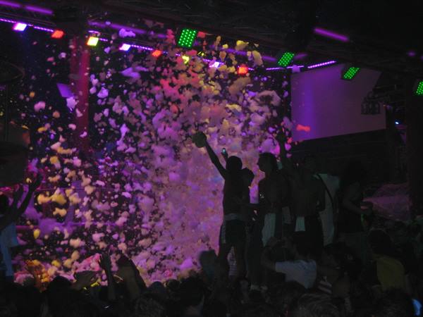 Nightclub foam party, purple foam falling on the crowd under LED lights
