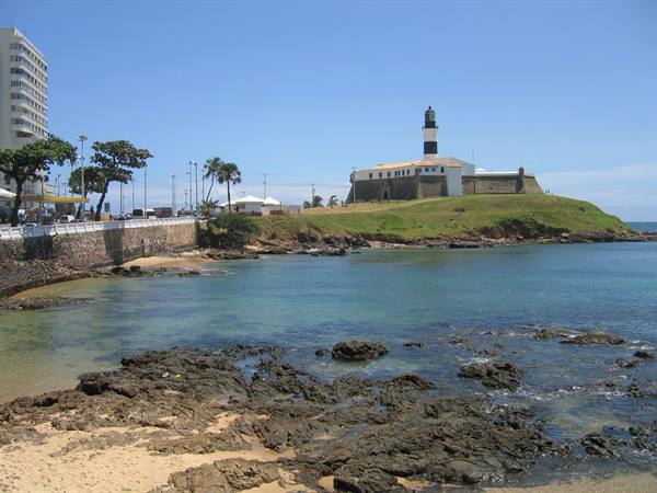 Barra Lighthouse in Salvador, turquoise sea between black rocks and palms under blue sky