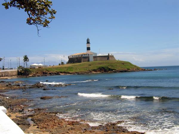 Barra Lighthouse in Salvador on green hill above rocks and waves