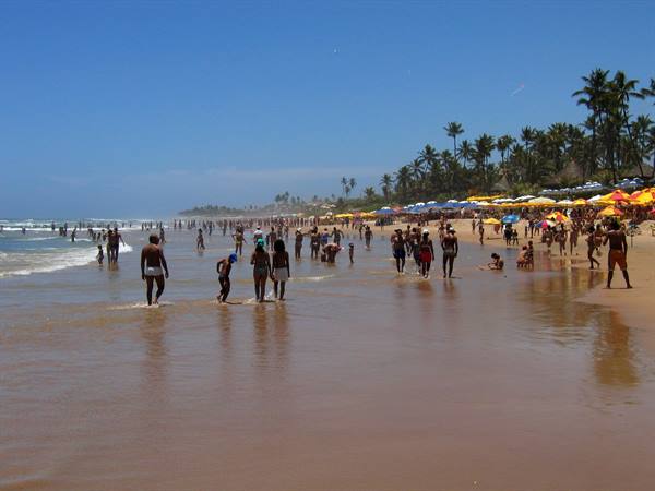 Bathers on wet sand at Praia do Forte, colorful umbrellas among palm trees
