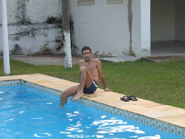 Man in swim trunks sitting at pool edge, feet in water