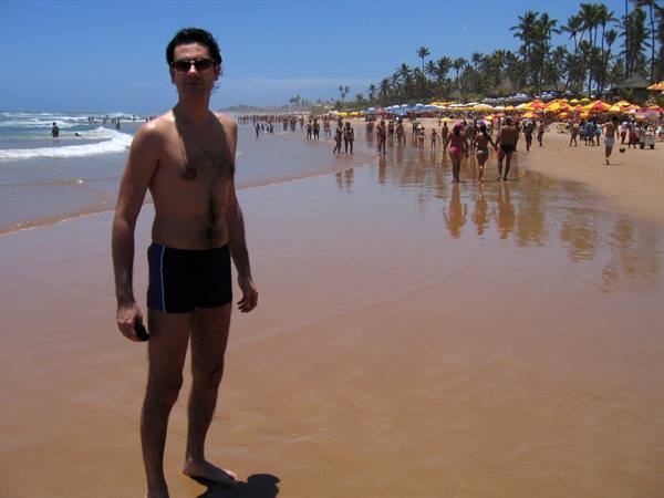 Man in swim trunks on crowded beach with umbrellas and palm trees