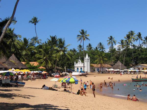 Swimmers on the beach in front of the white church at Praia do Forte, palms and umbrellas