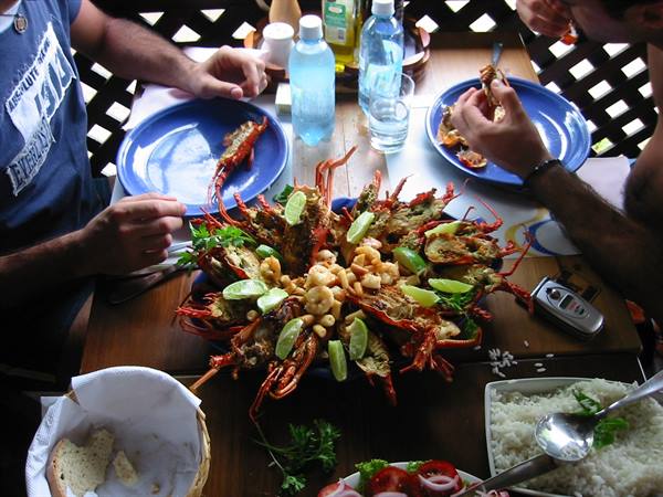 Wooden table with lobsters and lime centerpiece, friends eating with bread and rice