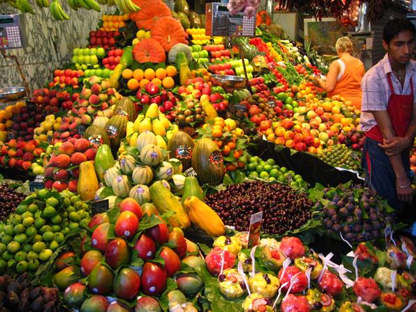 Colorful fruit stall at Barcelona's Boqueria market, vendor in red apron