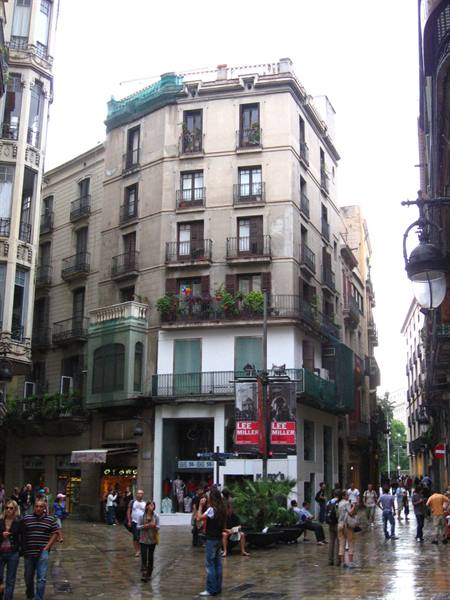 Tourists walk on a wet street in front of a building with balconies and flowers