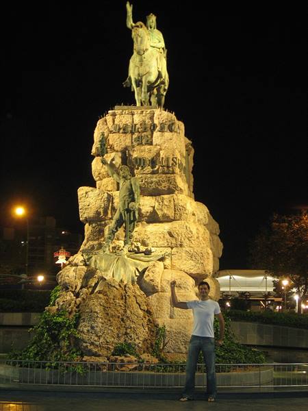 Tourist beside the stone monument of Ramon Berenguer III, lit up at night in Barcelona
