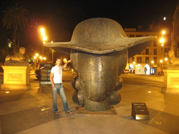 Tourist beside Botero's large bronze head, between illuminated stone sphinxes at night