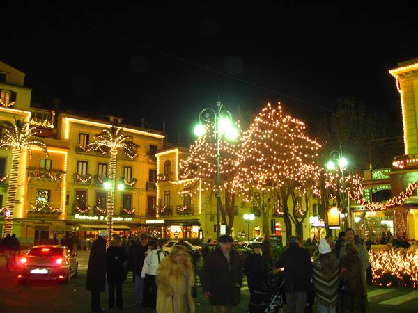 Festive lit square with palm trees wrapped in Christmas lights, people strolling