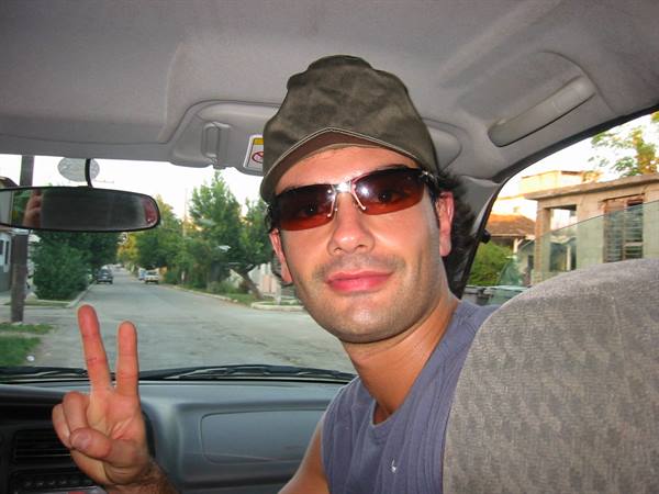 Man in cap and sunglasses makes peace sign inside a car