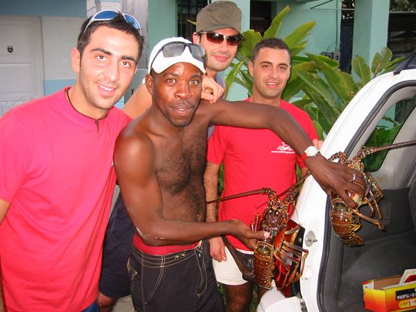 Four men by a white car, one holding two large lobsters just bought