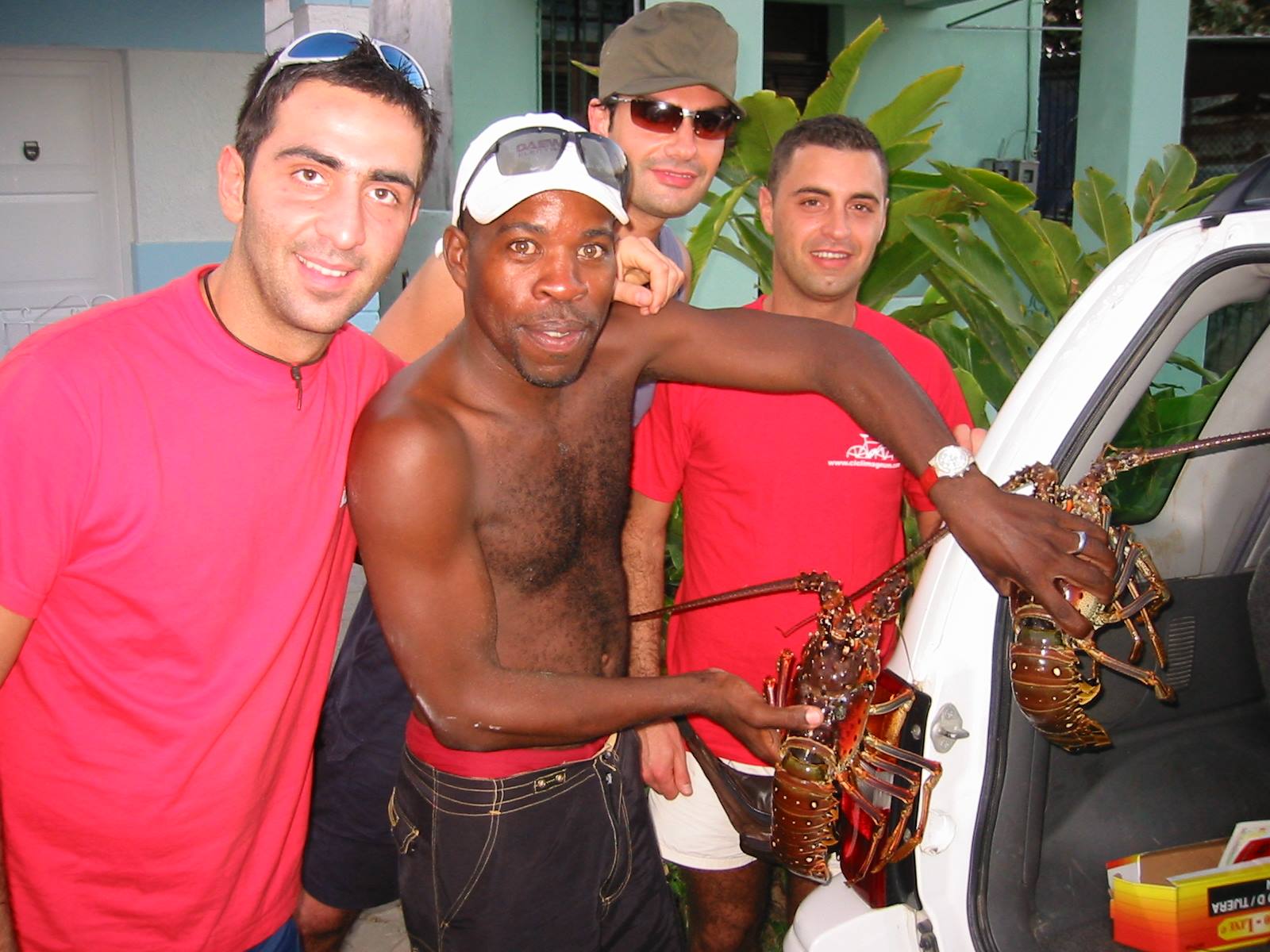 Four men by a white car, one holding two large lobsters just bought