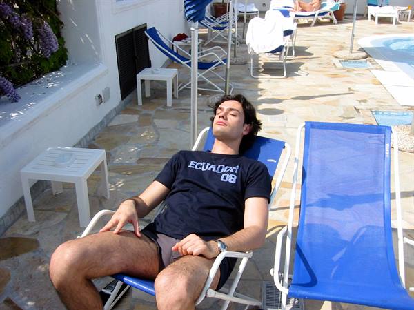 Young man sunbathing on blue lounge chair beside the pool