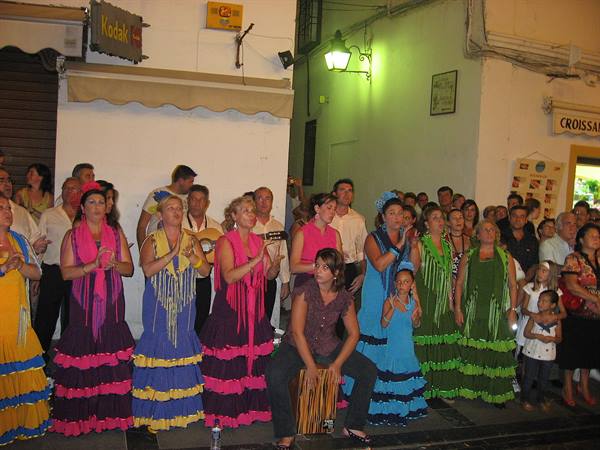 Women in colorful flamenco dresses clap at night among the crowd on a street