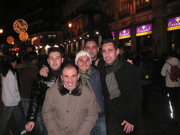 Five smiling friends on a crowded street at night, Christmas lights and lit signs