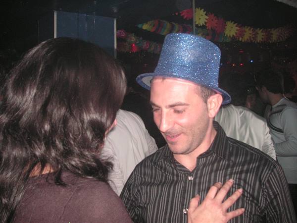 Man in blue glitter top hat dancing at crowded nightclub with colorful lights