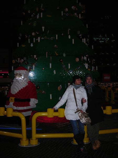 Couple beside Lego brick Christmas tree and Santa Claus at night