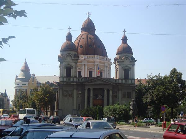 Church with copper domes and statue among parked cars under sunny sky