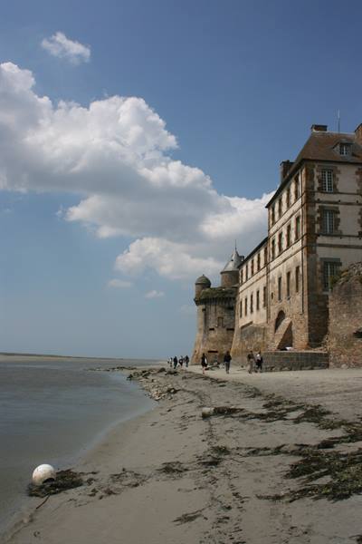 Tourists walk on the sand below the stone walls of Mont-Saint-Michel