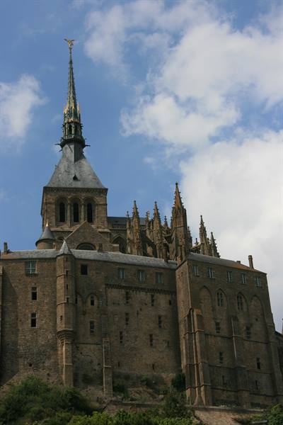 Mont-Saint-Michel abbey with golden spire above stone walls, white clouds
