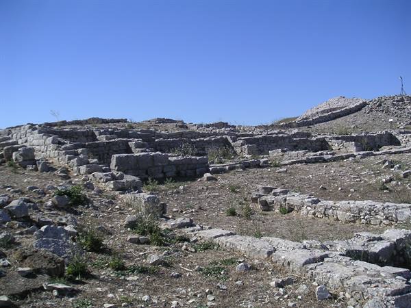 Ancient stone ruin walls under blue sky, scattered dry grass and rubble