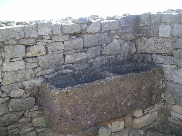 Ancient tufa stone basin set into a rough stone wall, natural light