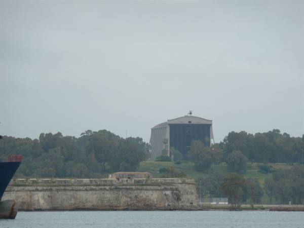 Seaplane hangar above old fortress walls, ships in harbor, grey sky