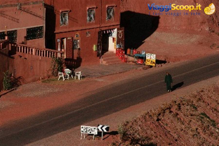 Woman in black walks along the road beside red earthen buildings, bright light