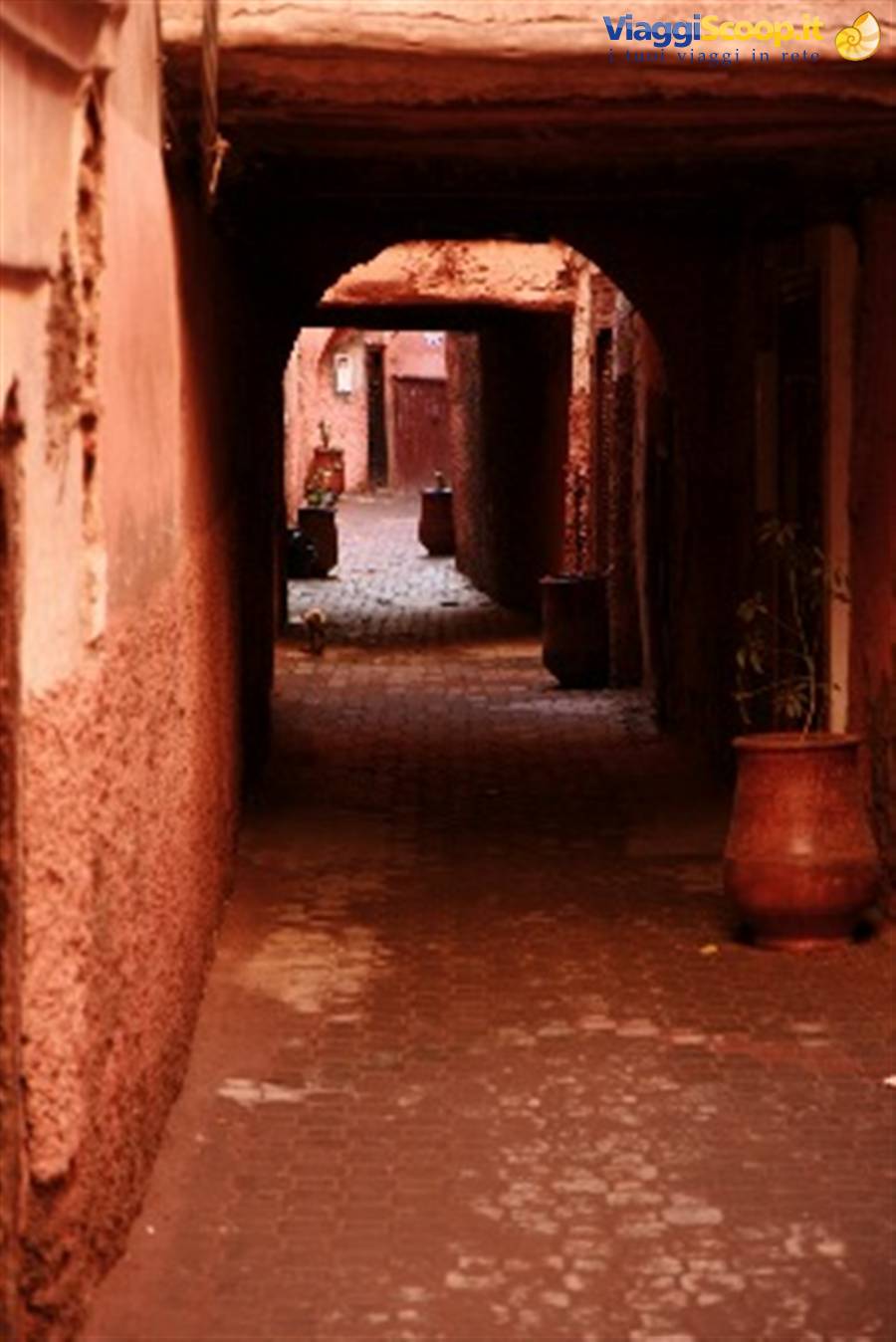 Red brick alleyway with arch and clay pots in the medina